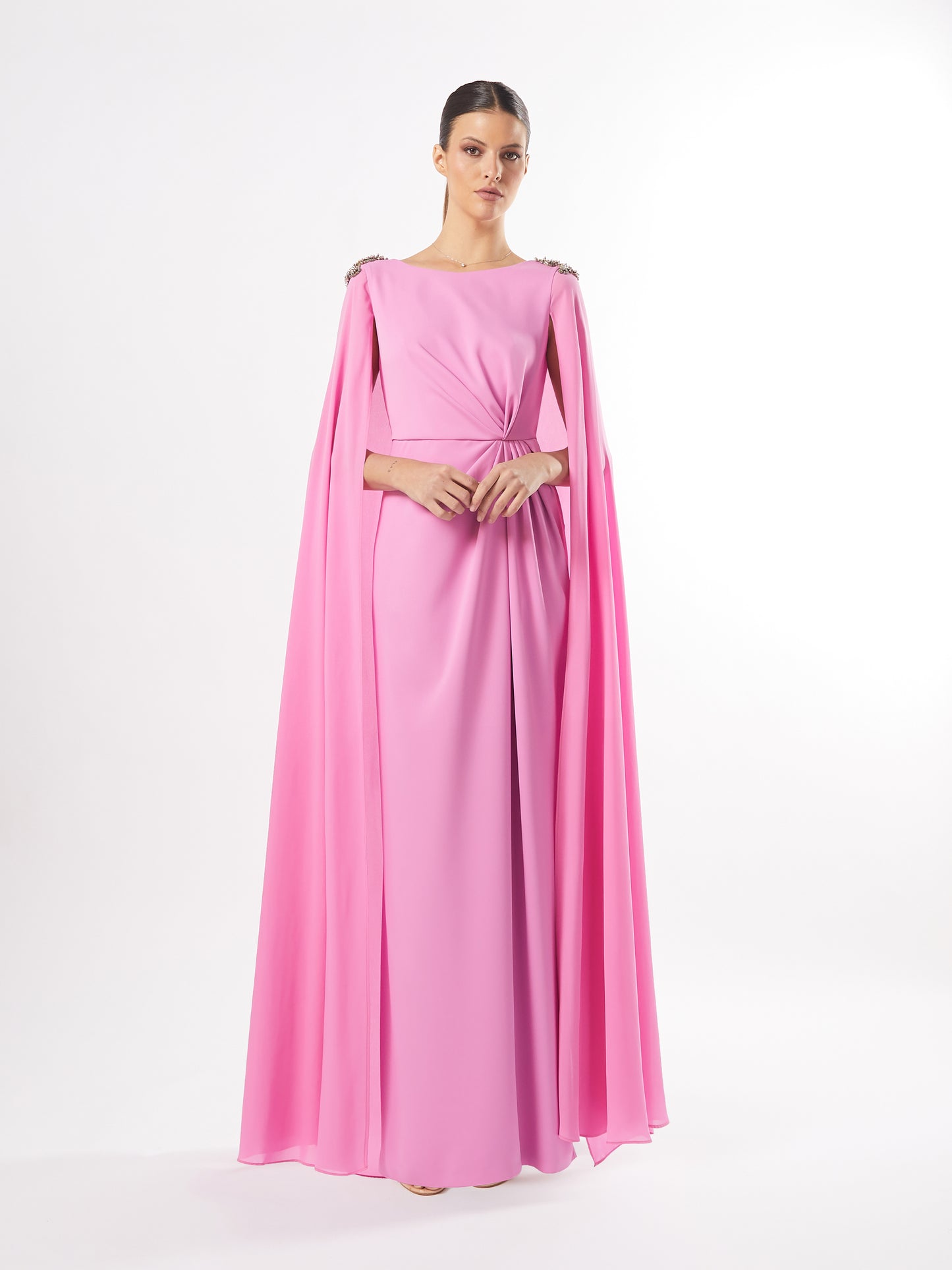 Model in a pink cape-sleeve evening gown with crystal shoulder embellishments, available in both pink and teal, against a white background.