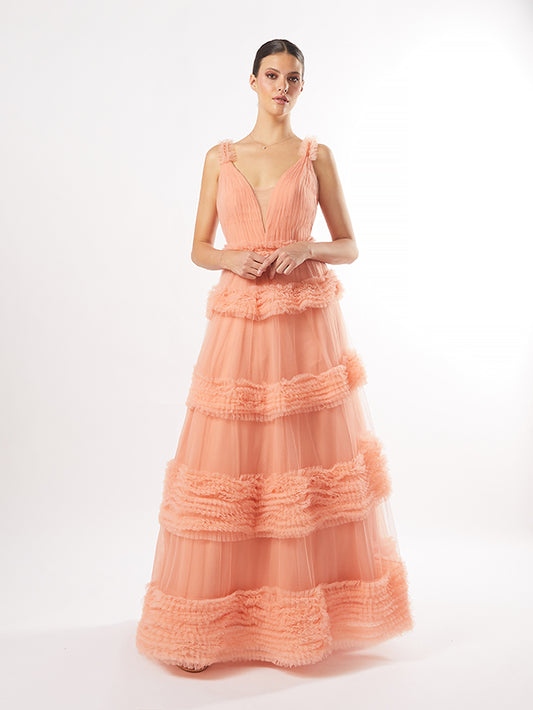 Model in a tiered peach tulle gown with textured fringes, available in peach, maroon, and pistachio, against a white backdrop.