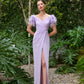 ront view of a model in a lilac (also available in dark fuchsia and turquoise) ruched evening gown with feathered shoulders and a deep V-neck.