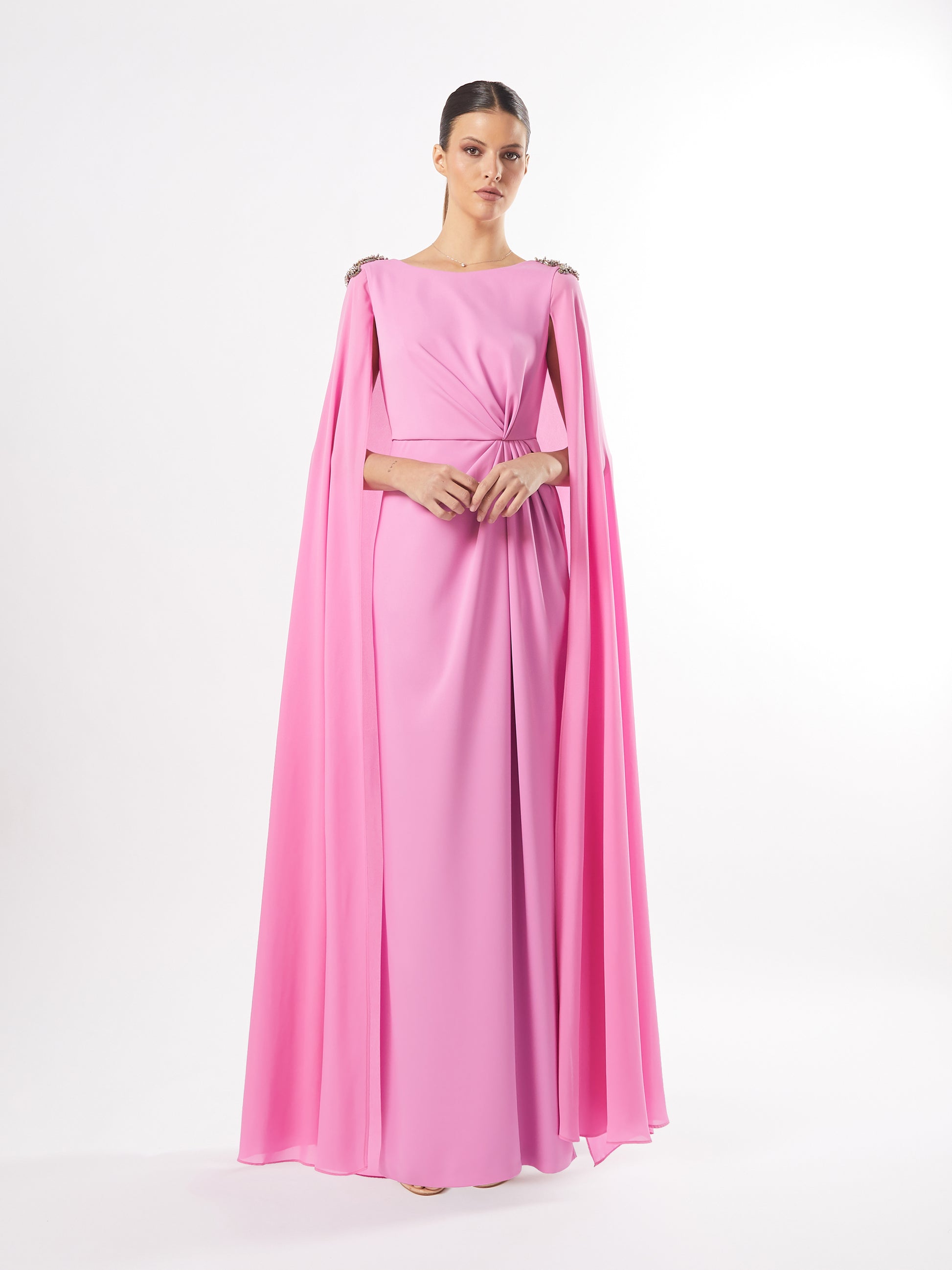 Model in a pink cape-sleeve evening gown with crystal shoulder embellishments, available in both pink and teal, against a white background.