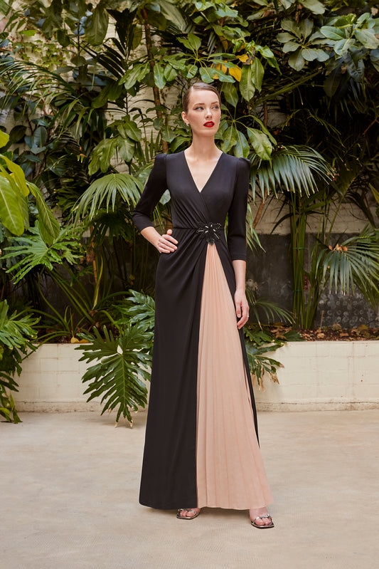 Front angle of an elegant two-tone black and beige evening gown with a deep V-neck and floral waist embellishment, modeled in a natural indoor setting.
