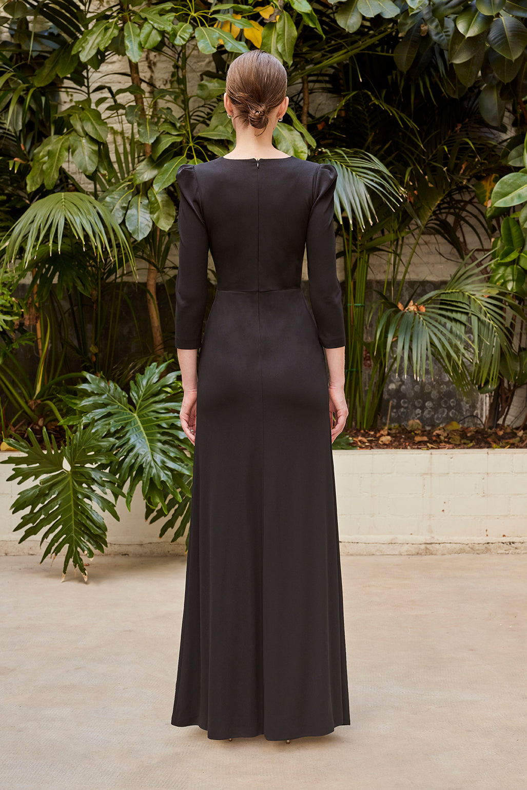 Back view of the elegant evening gown, highlighting the seamless zipper closure and the continuation of the sleek black fabric to the floor.