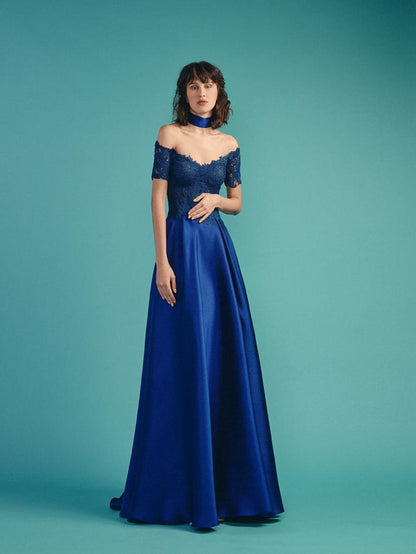 A woman in a royal sapphire blue gown with an off-the-shoulder lace bodice and a sleek satin skirt, complemented by a choker neckpiece against a teal backdrop