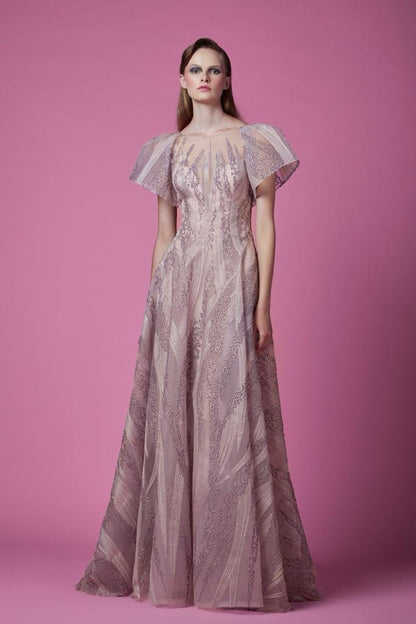 A woman stands poised in a blush tulle gown with embroidered detailing and ethereal puff sleeves, against a vibrant pink background.